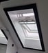 Ein schräges Dachfenster mit schwarzem Rahmen und weißer Verkleidung, das teilweise geöffnet ist.