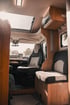Wohnmobil-Innenraum mit eleganten Holzmöbeln, moderner Beleuchtung und einer Sitzgruppe mit Stoffpolstern, ideal für Reisen und Komfort. 