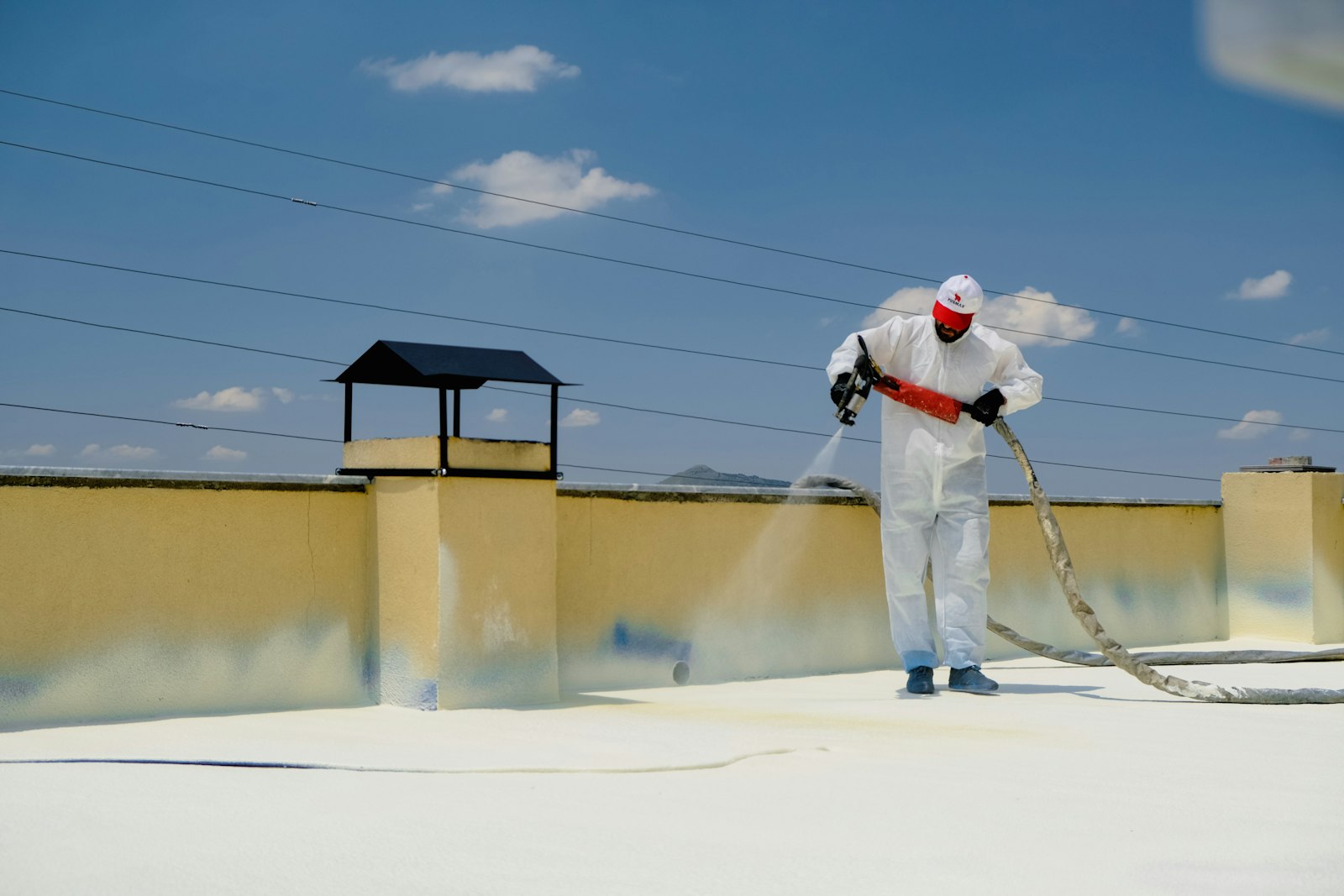 Worker spray-applying a liquid roof system on a low-slope roof, illustrating the silicone vs acrylic roof coating choice for Carrollton, TX buildings