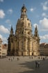 Die Dresdner Frauenkirche, eine barocke Kuppelkirche, steht auf einem belebten Platz unter blauem Himmel mit weißen Wolken.