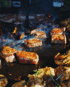 Steaks und Hähnchenstücke brutzeln mit aufsteigendem Rauch und Flammen auf einem großen, schwarzen Grill.