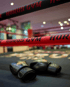 Schwarze Boxhandschuhe liegen auf dem Boden eines Boxrings mit roten Seilen, auf denen "HORUS GYM" steht.