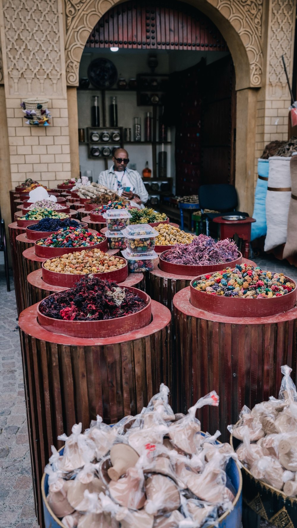 Marktstand mit Trockenblüten und Nüssen vor einem verzierten Torbogen