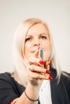 Blonde Frau mit roten Nägeln hält ein silbernes Permanent-Make-up-Gerät senkrecht in die Kamera.