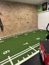 Fitnessstudio mit Ziegelwand, Kunstrasen-Bodenmarkierungen und Sportgeräten.