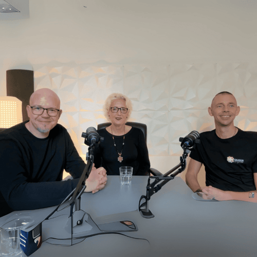 Three people, two men and a woman, sit at a table with microphones and smile at the camera.