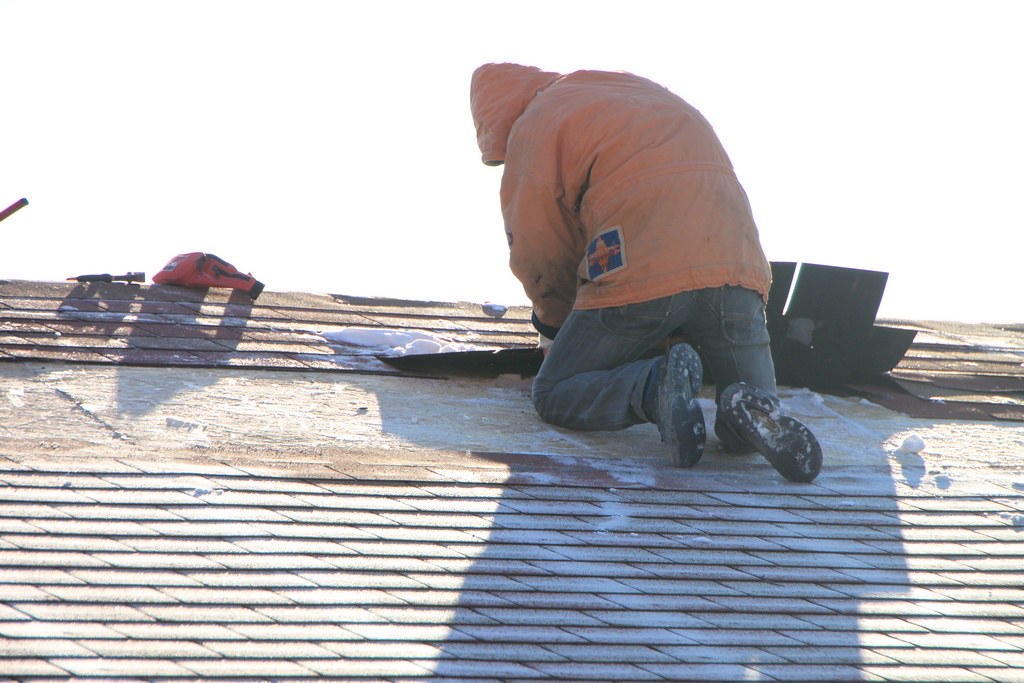Roofer kneeling on a shingle roof carrying out a targeted repair