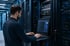 Mann mit Brille tippt auf Laptop vor Server-Racks in einem Rechenzentrum - Software-KRITIS Notfall- und Krisenmanager (NKM®).