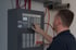 Matthias Hemminger bedient das Tastenfeld einer grauen Brandmelderzentrale an einer Wand mit sichtbaren Kabeln.