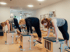 Drei Frauen trainieren in einem Studio an hölzernen Pilates-Stühlen und führen Stützübungen aus.