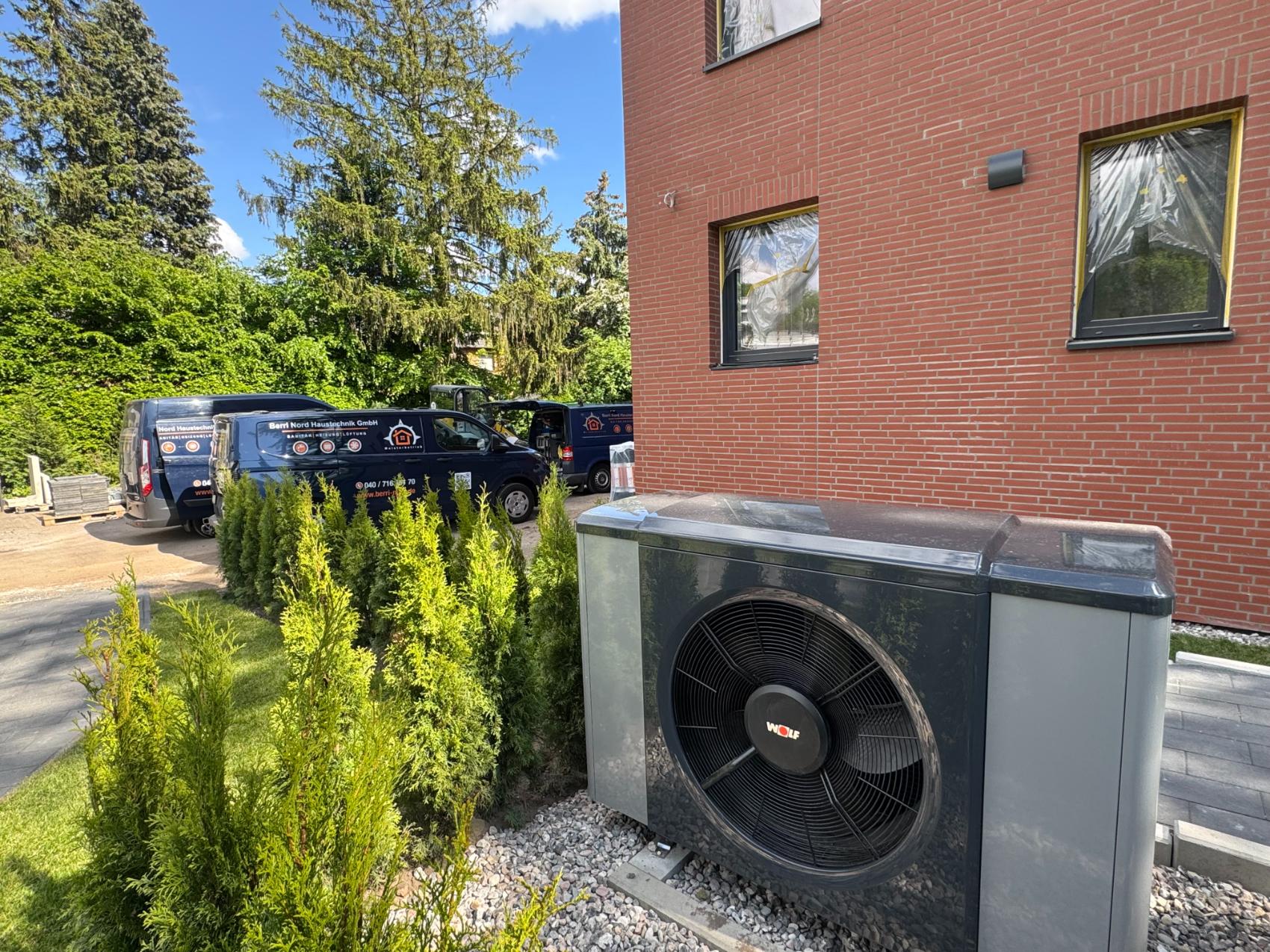 Luft-Wasser-Wärmepumpe an einem Neubau in Hamburg-Rahlstedt, im Hintergrund die Firmenwagen von Berri Nord Haustechnik
