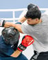 Zwei Boxer beim Sparring im Ring, einer trägt einen Kopfschutz und rote Boxhandschuhe.