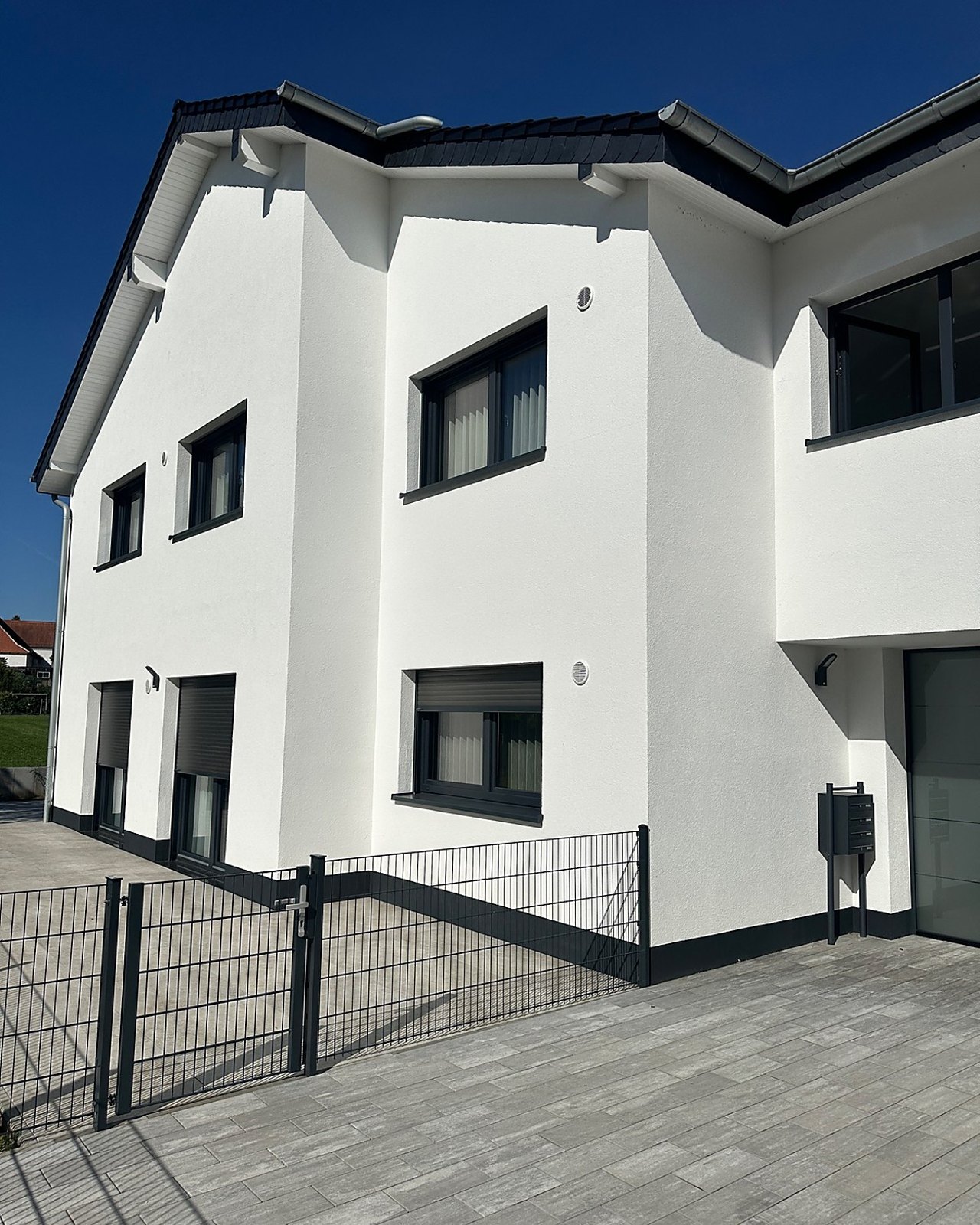 Fassadenansicht eines modernen Wohnhauses mit weißer Putzfassade und dunklen Fensterelementen.