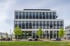 Modernes Bürogebäude mit dunkler Fassade, großen Fenstern, Parkplätzen und Bäumen davor.