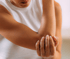 Woman in a white sleeveless shirt holding her elbow in pain.