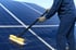 Person in blauer Arbeitskleidung und Handschuhen reinigt Solarmodule mit einer Bürste und Wasser.