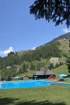 Freibad in Bergün mit blauem Schwimmbecken, Liegewiese und Rutsche, umgeben von grünen Berghängen unter blauem Sommerhimmel.