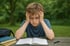 Junge mit zerzaustem Haar hält den Kopf in den Händen, während er ein offenes Buch auf einem Holztisch liest.