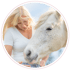 Blonde Frau in weißem T-Shirt füttert ein weißes Pferd mit der Hand.
