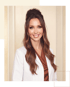 Smiling woman with long wavy brown hair wearing a white lab coat over a brown top.