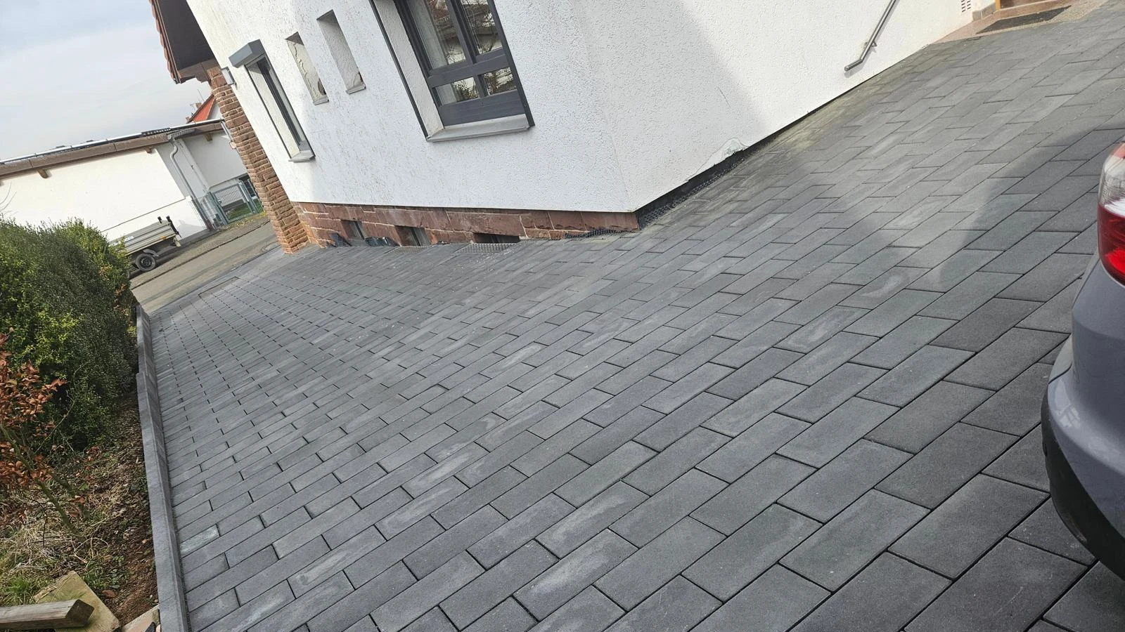 Fertig gepflasterte Einfahrt in Anthrazit, seitlich am Haus, mit gesetzter Randsteinkante zum Beet