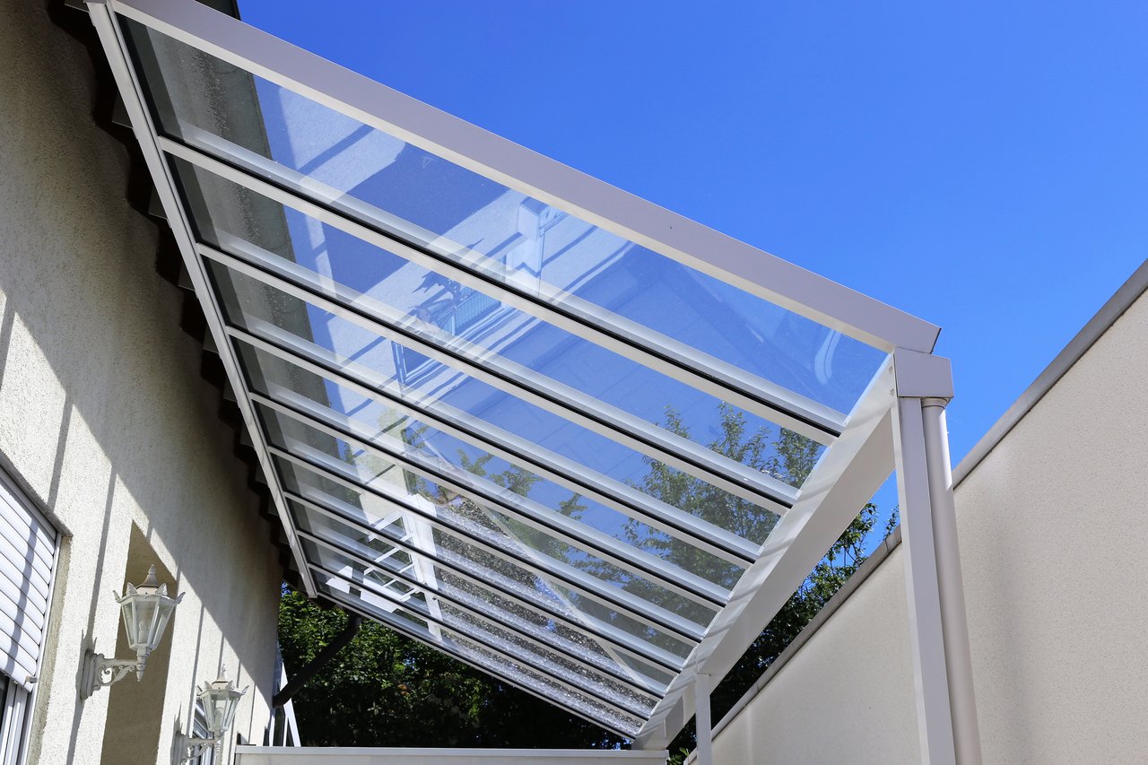 Terrassendachreinigung in Marzahn-Hellersdorf: Überdachung aus Glas und Aluminium vor blauem Himmel.