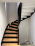 Moderne Wendeltreppe mit Holzstufen, schwarzer Wange und Handlauf in einem hellen Treppenhaus mit Kerzendekoration.