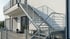 Außenliegende, verzinkte Stahltreppe mit Geländer an einem weißen Gebäude.