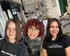 Drei Frauen lächeln in einem Friseursalon, zwei tragen schwarze Paul Mitchell T-Shirts.