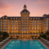 Large luxury hotel with a domed tower, illuminated windows, and a swimming pool at sunset.