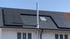 Dach mit schwarzen Solarmodulen, Schornstein, Dachfenster und weißer Fassade.