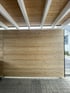 Ein Carport mit einer Sichtschutzwand aus horizontalen Holzlamellen unter einer Decke mit weißen Holzbalken.