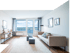 Modernes helles Wohnzimmer mit beigem Sofa, Teppich, Holzregal und großem Fenster mit Balkonzugang.