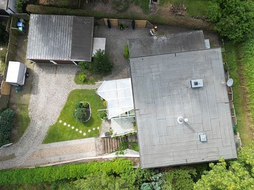 Luftaufnahme eines Hauses mit Flachdach, großem Garten, Garage und Gewächshaus.