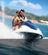 Mann und Frau tragen Schwimmwesten auf einem Jetski, der auf dem Wasser Wellen schlägt.