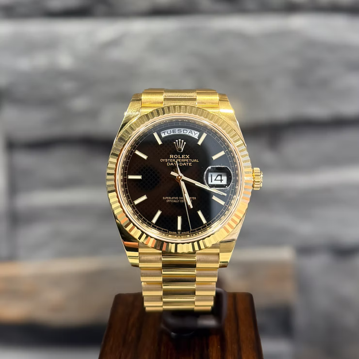 Goldene Rolex Oyster Perpetual Day-Date Armbanduhr mit schwarzem Zifferblatt und Datumsanzeige auf Holzständer.