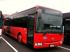 Roter Reisebus mit offener Tür, geparkt auf einem Asphaltplatz mit weißen Linien.