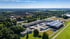 Luftaufnahme einer Fabrikanlage mit mehreren Gebäuden, LKWs und Solarpaneelen unter blauem Himmel.