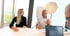 Zwei Personen sitzen an einem Konferenztisch; eine blonde Frau und ein grauhaariger Mann, der gestikuliert.