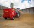 Roter Teagle Futtermischwagen verteilt Stroh neben einem blauen Traktor auf einem Bauernhof.
