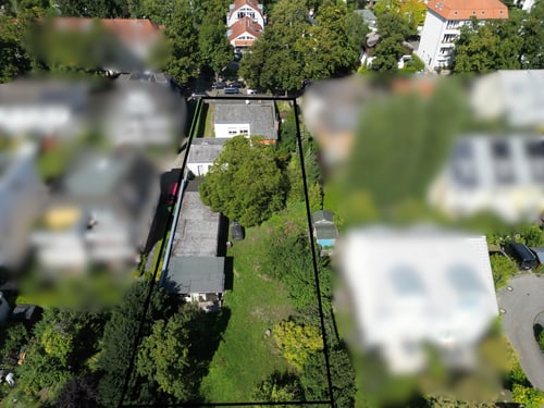 Luftaufnahme eines schmalen, langen Grundstücks mit zwei Häusern und Bäumen, umrandet von einer schwarzen Linie.