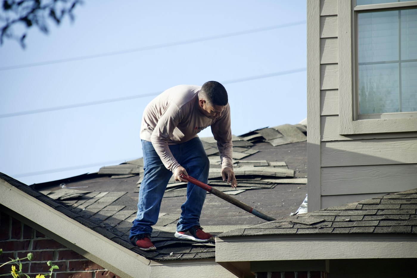 Roofer stripping old shingles from a residential roof deck
