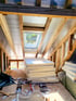 Dachausbau mit sichtbaren Holzsparren, eingebautem Dachfenster und gestapelten Dämmplatten auf einer Baustelle.
