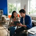 A man and woman sit together in a modern living room looking at a digital tablet.