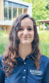 Lächelnde Frau mit lockigem Haar und blauem Poloshirt mit "KEIDEL FREIBURGS THERME"-Logo.