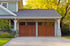 A light green house with two wooden garage doors and a concrete driveway.