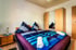 Doppelbett mit blauen Kissen und Decken, Holzschrank mit Spiegeln und Nachttisch in einem Schlafzimmer.