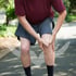 Man outdoors clutches his painful, inflamed knee while seeking relief.