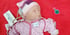 Bild zeigt die kleine Frühchenpuppe Lewis vom Bundesverband "Das Frühgeborenen Kind e.V." welches in einen Body von meinmaikaempfer in der Größe 32 eingekleidet ist. Sie trägt außerdem eine Mütze von meinmaikaempfer in rosa gestreift mit einem Kopfumfang von 26 cm.
