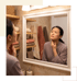 A woman in a robe examines her neck in a bathroom mirror, touching her throat with a concerned expression.
